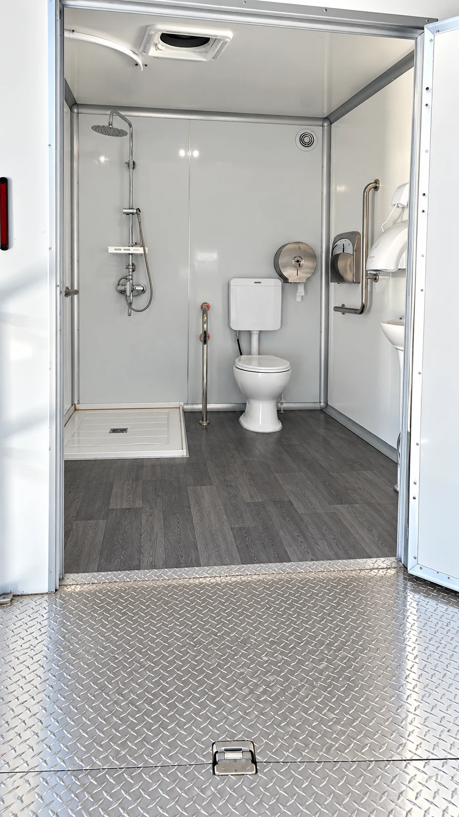 Wide entrance to a shower-restroom trailer room with grab bars, toilet and open shower floor